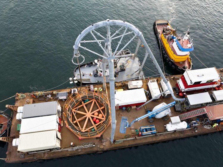 Aerial view of a barge at Port of Seattle’s Pier 66, featuring a cable buoy system, shipping containers, and a support tugboat in the water.